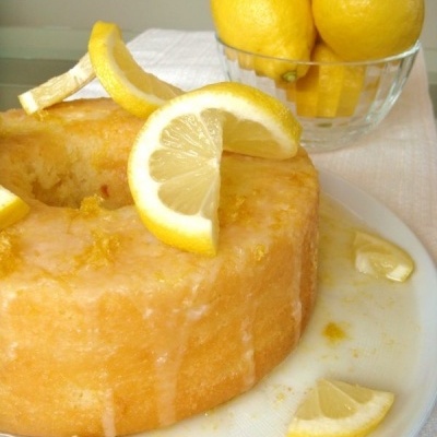 Bolo redondo decorado com fatias de limão ao lado de uma taça com limões amarelos