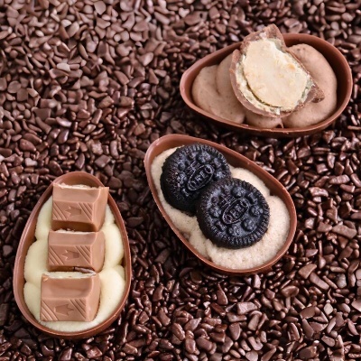 Ovos de chocolate recheados com pedaços de chocolate, bolachas OREO e recheio cremoso sobre granulado de chocolate.