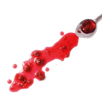 Colher com geleia vermelha e pedaços de fruta sobre superfície branca