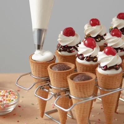 Cones de gelado decorados com chantilly, chocolate e cerejas vermelhas numa estrutura metálica