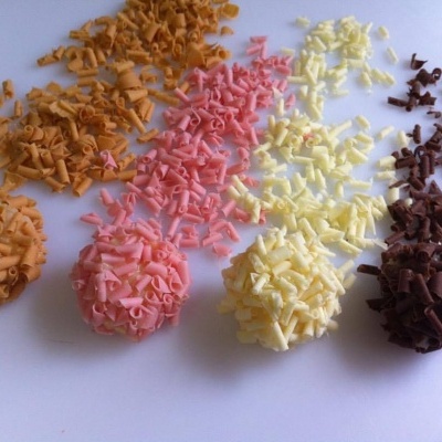 Cinco colheres com lascas coloridas de chocolate em pó sobre fundo branco