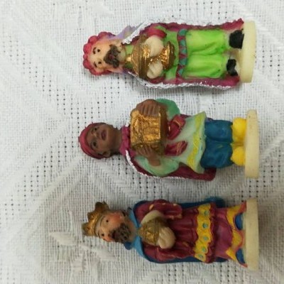 Três figuras decorativas de Reis Magos em resina coloridas sobre toalha branca