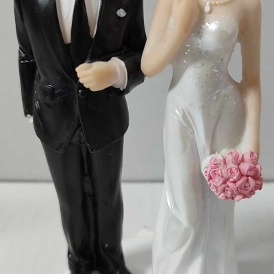 Estatua decorativa de casal de noivos, noivo de fato preto e noiva de vestido branco com bouquet rosa