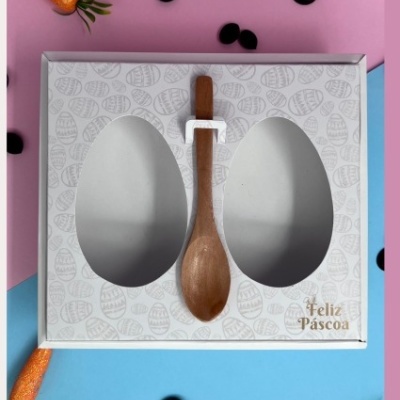 Caixa branca para ovos de Páscoa com colher de madeira, decorada com mini cenouras e círculos pretos num fundo rosa e azul