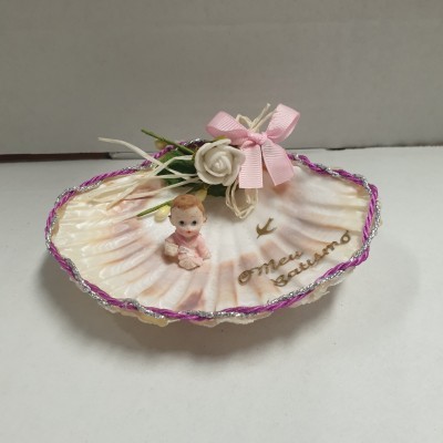 Concha decorativa com figura de bebé, flor artificial, laço rosa e texto 'Meu batizado'.