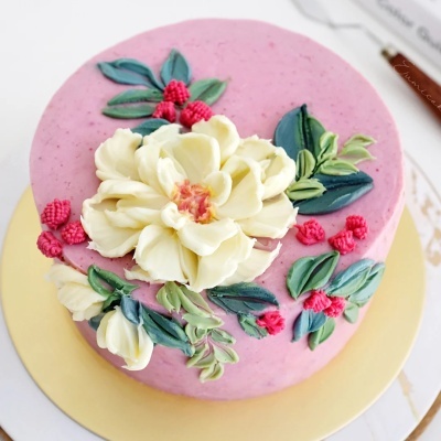 Bolo decorado com flores de creme e frutos vermelhos sobre cobertura rosa