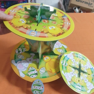 Estrutura de papel com pintainhos, coelhos e ovos de Páscoa coloridos, em duas camadas circulares, sobre mesa laranja.