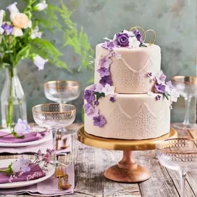 Bolo de casamento branco com decoração lilás em mesa rústica