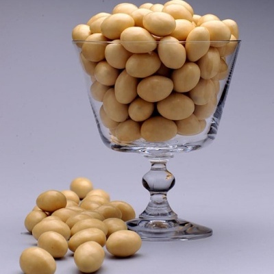 Taça de vidro cheia de amêndoas revestidas bege com amêndoas ao lado, fundo cinzento.