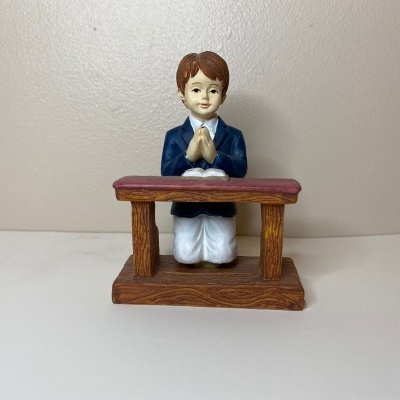 Figurina de criança ajoelhada a rezar diante de móvel de madeira