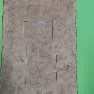 Peça transparente retangular com recortes e texto Alliantech A007 sobre fundo verde