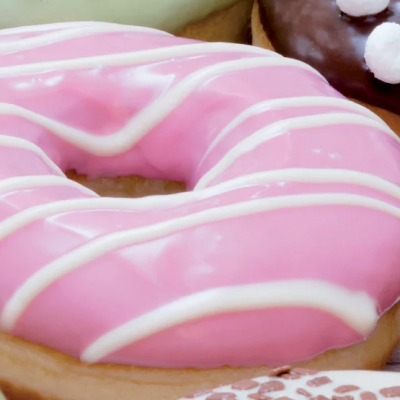Donut com glacê rosa e riscas brancas em embalagem junto a outros donuts
