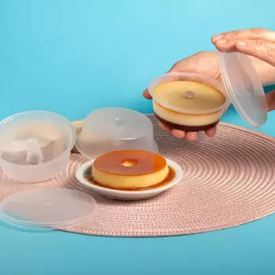 Pudim caramelizado em recipiente plástico e prato sobre tapete claro com fundo azul
