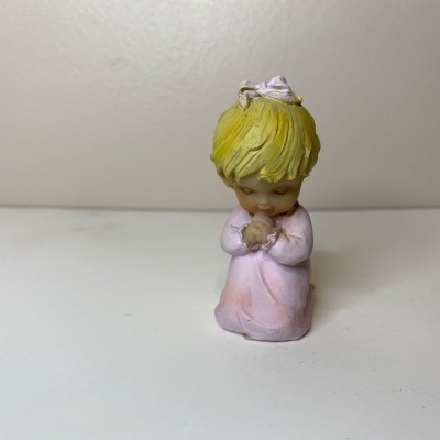 Figurinha pequena de criança a rezar com vestido rosa e cabelo amarelo
