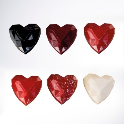 Seis chocolates em forma de coração facetados em várias cores sobre fundo branco.