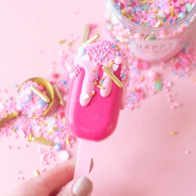 Gelado cor-de-rosa com cobertura de granulados coloridos e decoração, mão segurando, fundo rosa