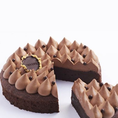 Bolo redondo de chocolate com cobertura cremosa em picos e bolinhas de chocolate.