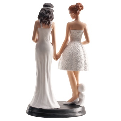 Estatuetas de duas mulheres de mãos dadas, uma de vestido longo branco e outra de vestido curto branco, com cão ao lado