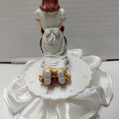 Figura de menina ajoelhada em vestido branco sobre base com tecido branco acetinado