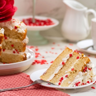 Fatia de bolo de camadas com creme branco e decorações vermelhas e douradas num prato branco