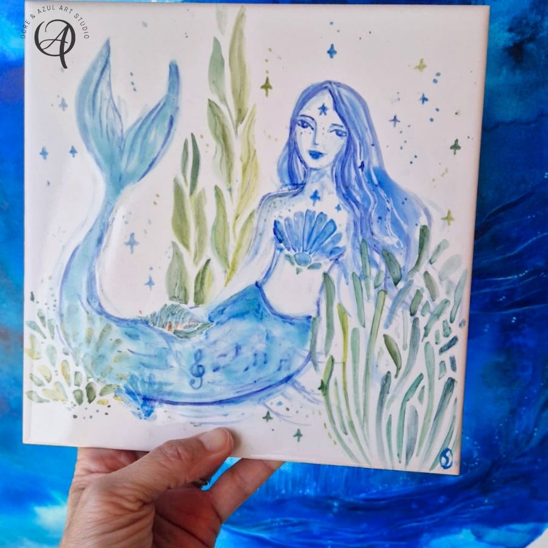 Azulejo Sereia I Azulejo decorativo com ilustração de sereia azul e plantas aquáticas verdes.