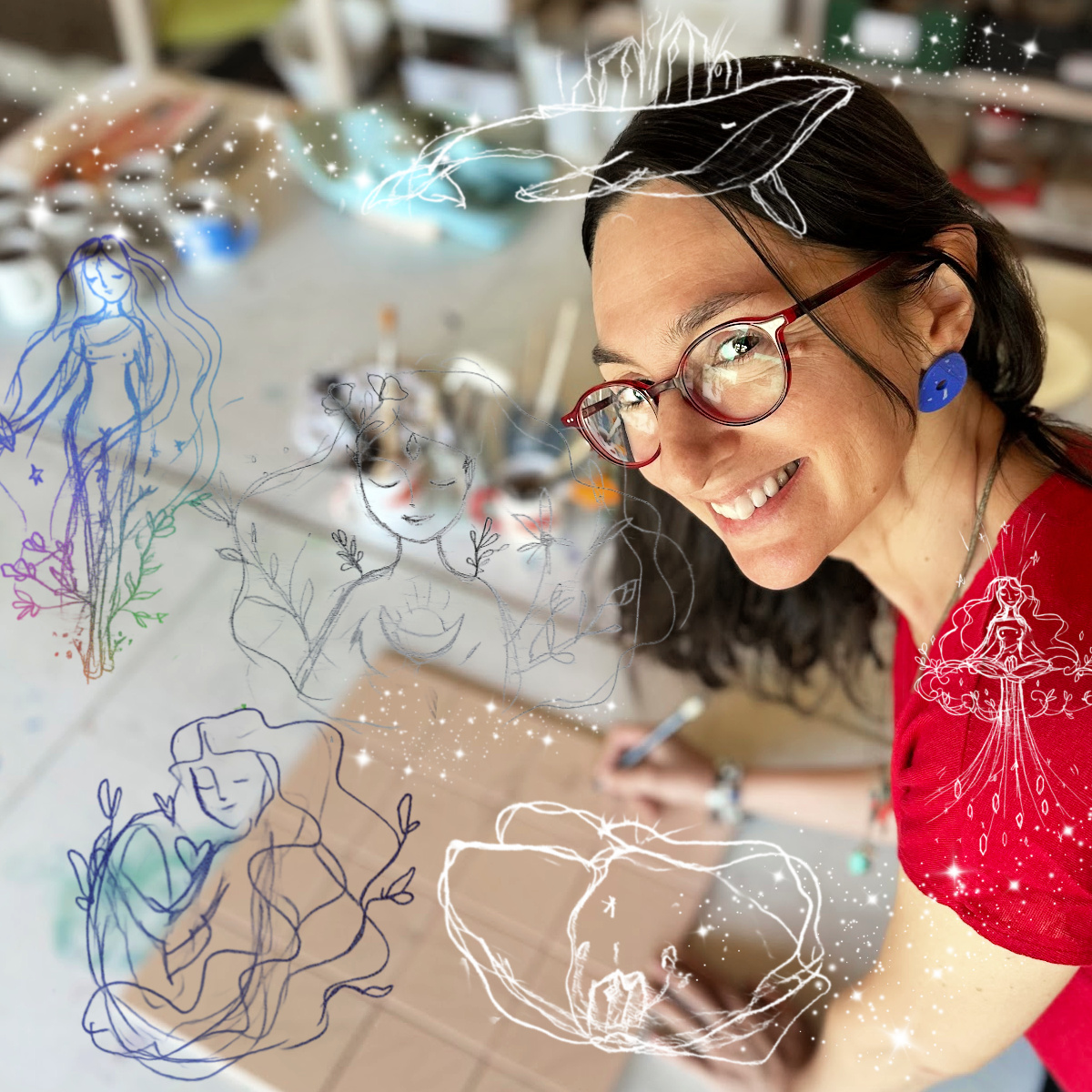 Sara, a artista contadora de histórias! Mulher com óculos vermelhos, brincos azuis e camisa vermelha a desenhar numa mesa de trabalho