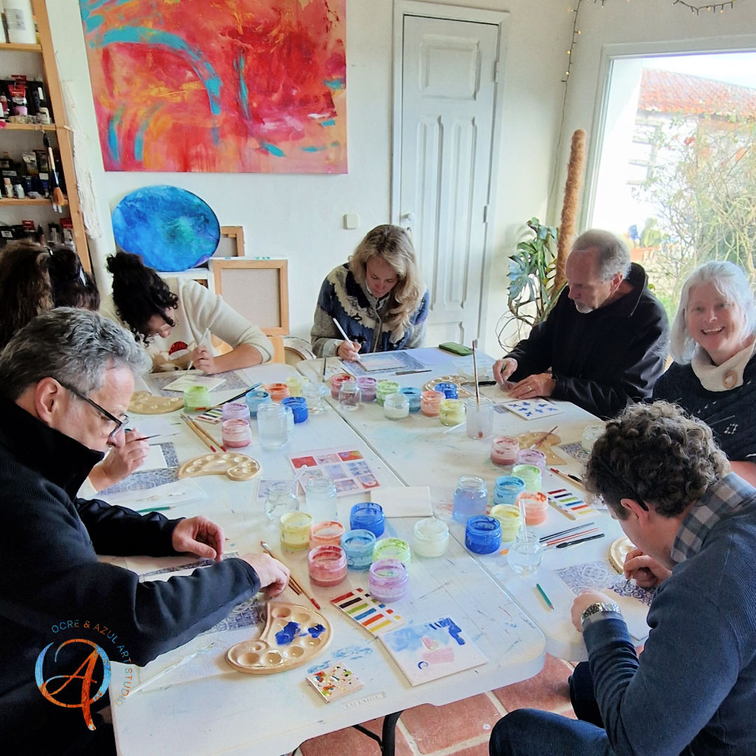 Tile Painting Workshop Pessoas a pintar numa mesa com tintas coloridas em estúdio de arte