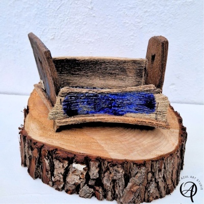 Miniatura de cama rústica em madeira envelhecida com pintura azul colocada sobre tronco de árvore