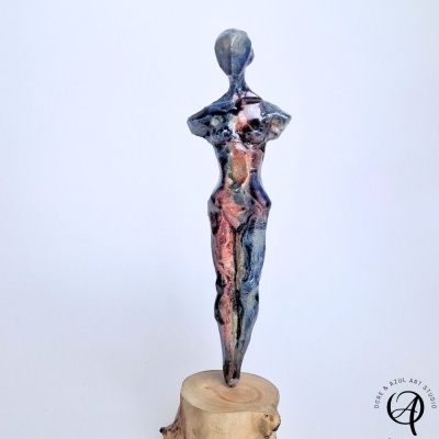 Escultura abstrata de figura humana em tons metálicos sobre base de madeira rústica