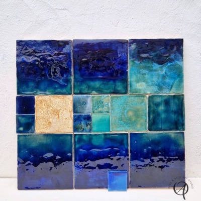 Azulejos de cerâmica vidrada azuis, verdes e bege numa parede branca com selo no canto inferior direito