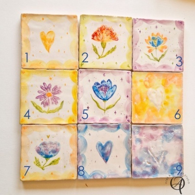 Azulejos quadrados pintados à mão com números e desenhos de corações e flores coloridas.