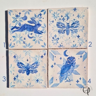 Quatro azulejos decorativos quadrados com desenhos em azul e branco mostrando coelho, abelha, mariposa e coruja com estrelas e flocos de neve