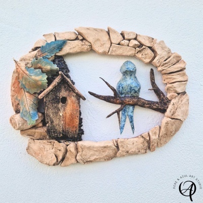 Ornamento de parede com casinha de madeira, folhas coloridas e pássaro azul em estrutura de pedra bege.