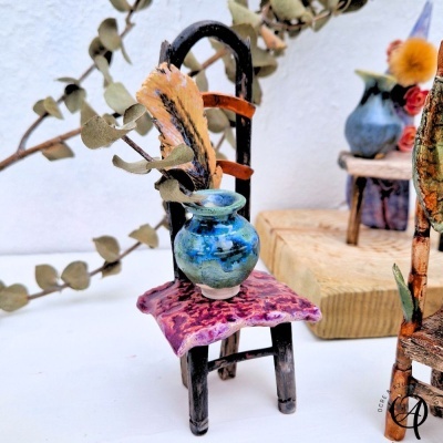 Mini cadeira de madeira preta com almofada roxa e vaso cerâmico azul no assento com folha seca.