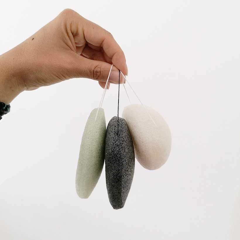 Esponjas Konjac - Croll & Denecke Três pedras de escudo facial penduradas em cordões seguradas por uma mão