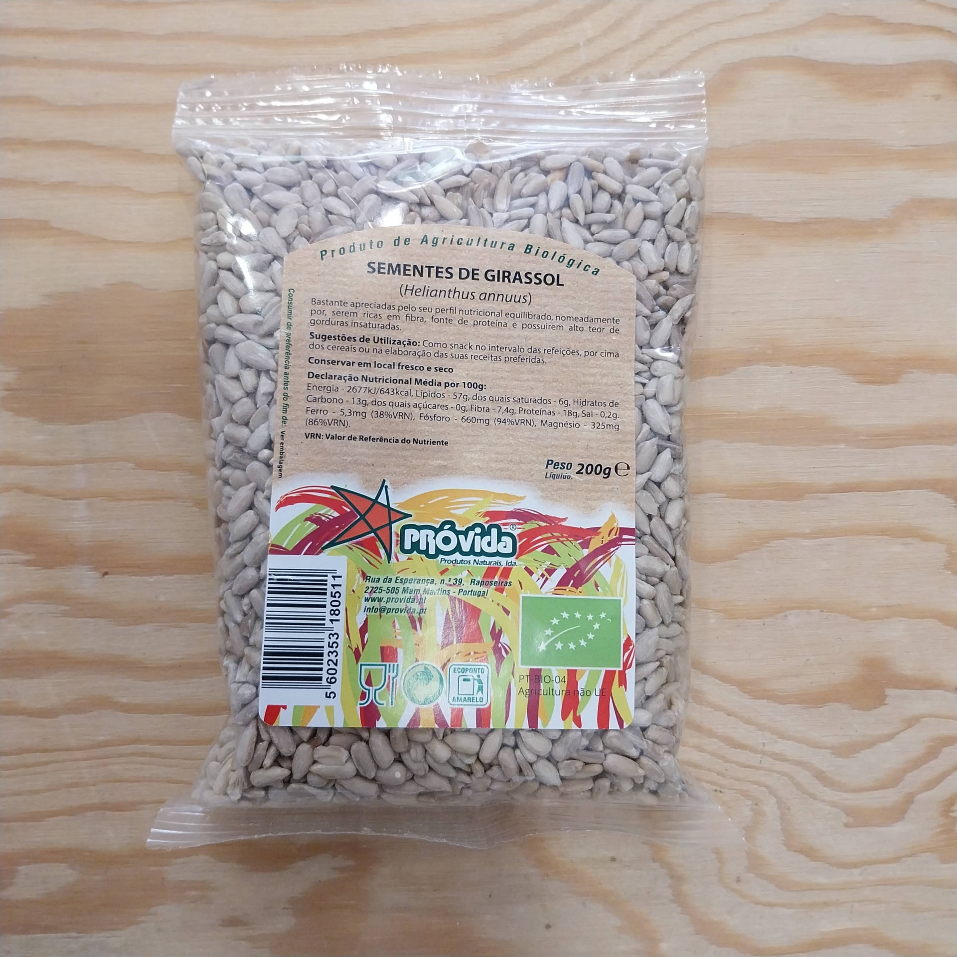Sementes de Girassol BIO - Granel Pacote de sementes de girassol Próvida em plástico transparente com rótulo informativo em fundo de madeira clara
