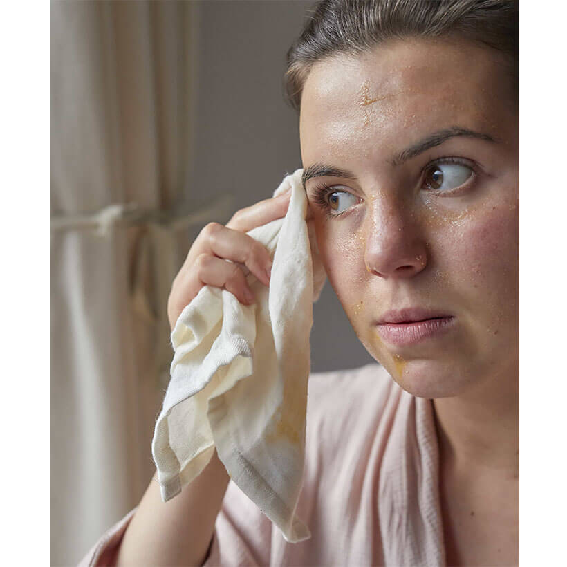 Mulher limpa o rosto com pano branco em ambiente interior