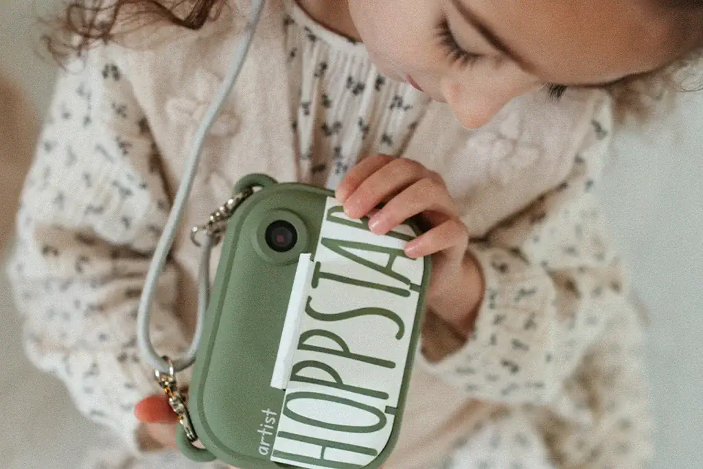 Máquina Fotográfica Digital Artist Laurel - Hoppstar Criança a segurar carteira verde com etiqueta HOPPSIA