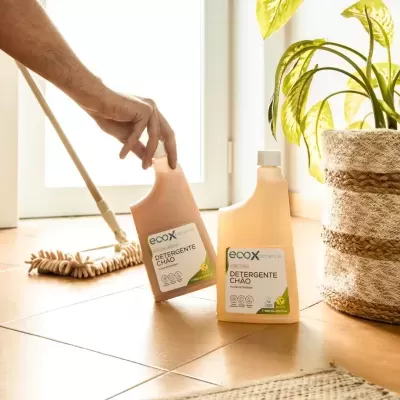 Dois frascos de detergente para chão ecox num chão de azulejos junto a planta e vassoura