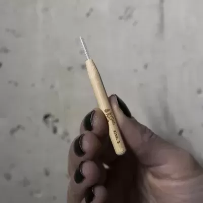 Mão segurando escova interdental com cabo de madeira