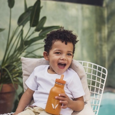 Criança sorridente com garrafa laranja sentada numa cadeira branca junto à piscina