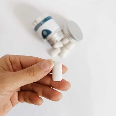 Mão segurando cápsula branca com frasco ao fundo