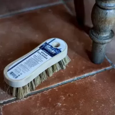 Escova de limpeza branca com cerdas naturais sobre chão de azulejos castanhos