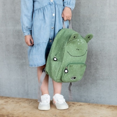 Mochila verde com rosto sorridente sendo segurada por criança com vestido azul