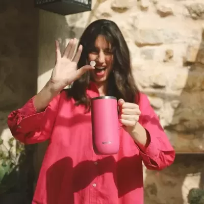 Mulher com camisa vermelha segurando caneca térmica rosa com logo ONEISALL