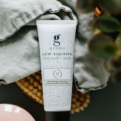 Frasco de produto de cuidados faciais grums raw espresso com texto, em fundo de toalha cinzenta e planta verde.