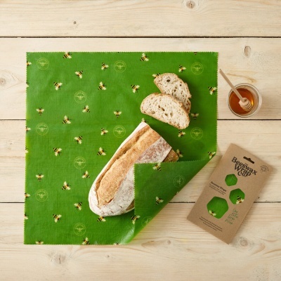 Pano verde com padrão de abelhas a embrulhar pão sobre mesa de madeira clara