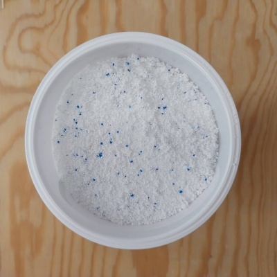 Pote branco com detergente em pó branco e partículas azuis sobre madeira clara