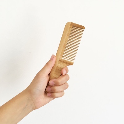 Pente de madeira natural segurado por uma mão contra fundo branco