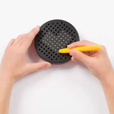 Objeto circular preto com furos nas mãos sobre fundo branco.